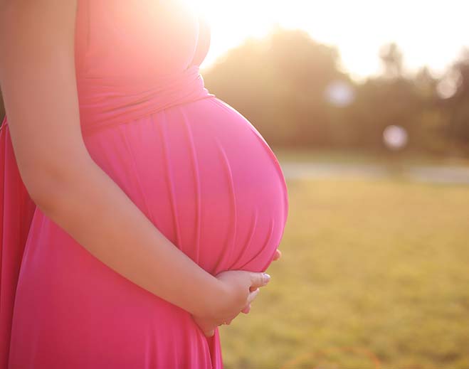 Pregnant person holding belly outdoors at sunset