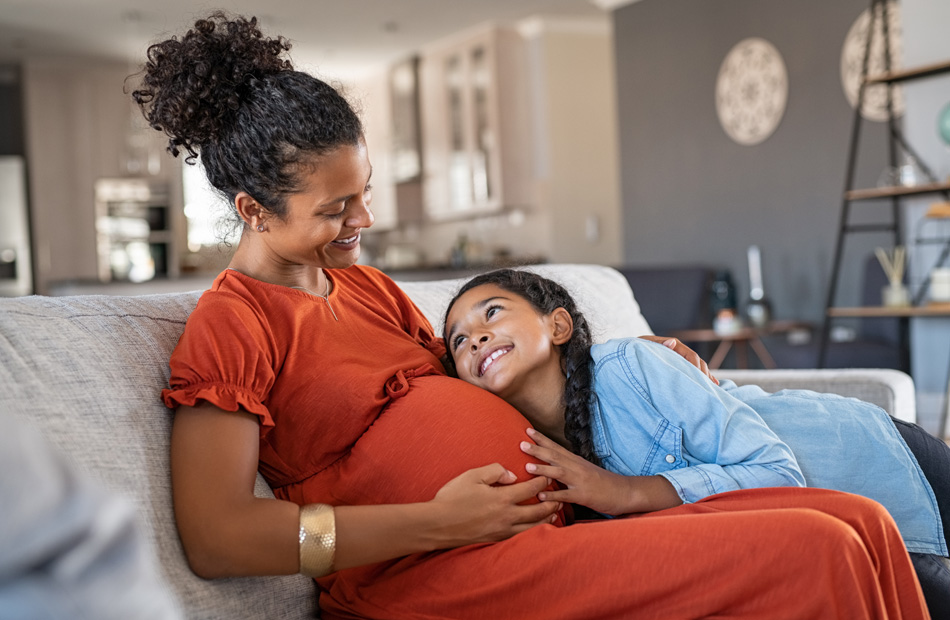 Pregnant person resting while child hugs belly