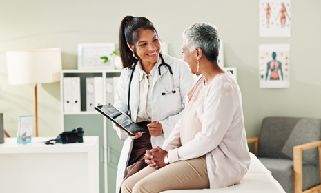 A doctor holds a tablet computer and discusses medical care options with a patient
