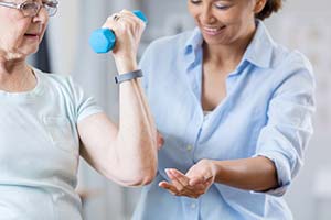 therapist helping elderly woman lift weights