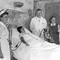 Patient lying in a hospital bed with a nurse, doctor, and visitor